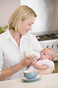 Mother feeding baby in kitchen with coffee smiling