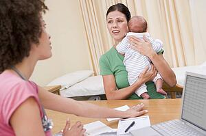 Doctor with laptop and woman in doctor's office holding baby