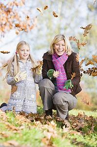 Woman and young girl outdoors in park playing in leaves and smiling (selective focus)