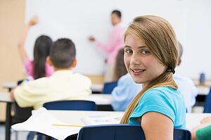 Student in class looking at camera with teacher in background (selective focus)