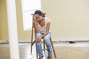 Woman sitting on ladder in empty space looking tired