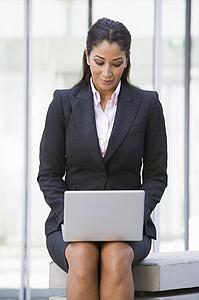 Businesswoman sitting outdoors by building with laptop (high key/selective focus)