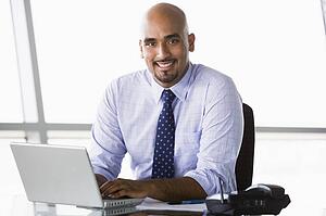 Businessman in office with laptop smiling (high key/selective focus)