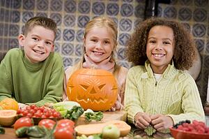 Three young friends on Halloween with jack o lantern and food smiling