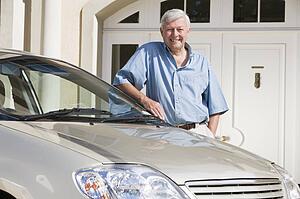 Senior man standing with his car outside his home