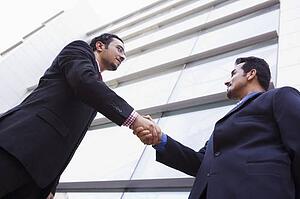 Two businessmen outdoors by building shaking hands (high key/selective focus)