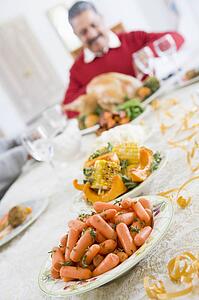 Dinner Table With Christmas Dishes, With Man In Background Carving Turkey