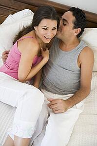 Couple relaxing on bed in bedroom snuggling and smiling (selective focus)