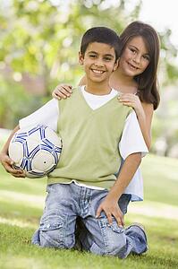 Two young children outdoors in park with ball smiling (selective focus)