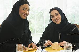 Two women sitting at dinner table smiling (high key)
