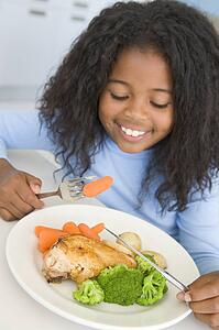 Young girl in kitchen eating chicken and vegetables smiling