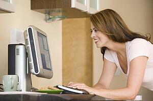 Woman in kitchen with computer smiling