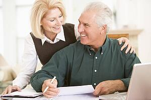 Couple in dining room with laptop and paperwork smiling