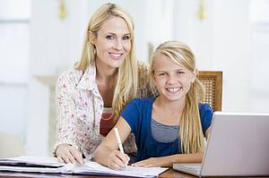 Woman helping young girl with laptop do homework in dining room