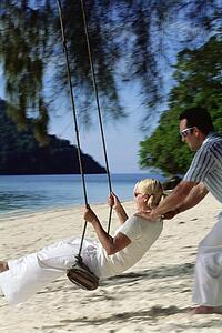 Man outdoors by a beach pushing a woman on a swing (selective focus)