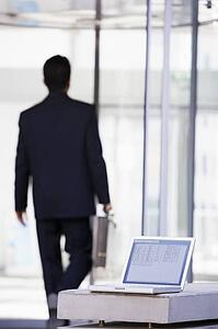 Laptop sitting on stone bench outdoors with businessman walking away in background (high key/selective focus)