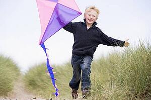 Young boy running on beach with kite smiling