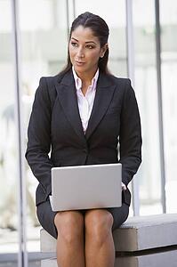 Businesswoman sitting outdoors by building with laptop (high key/selective focus)