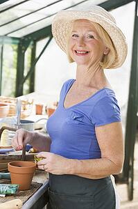 Woman in greenhouse putting seeds in pot and smiling