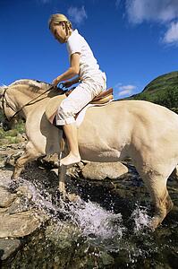 Woman outdoors riding horse through stream (fisheye)