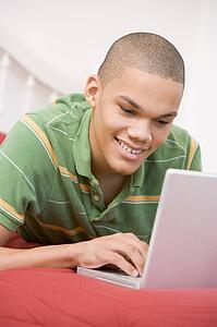 Teenage Boy Lying On Bed Using Laptop 