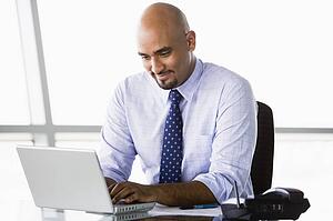 Businessman in office with laptop smiling (high key/selective focus)