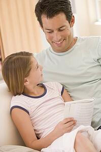 Man and young girl in living room reading book and smiling
