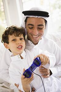 Father and son in living room playing video games and smiling (high key/selective focus)