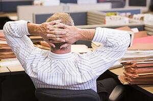 Businessman in cubicle with laptop and stacks of files