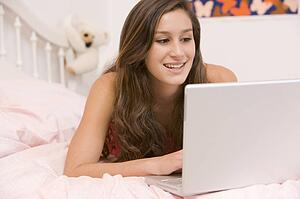 Teenage Girl Lying On Her Bed Using Laptop