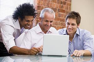 Three businessmen sitting in office with laptop smiling