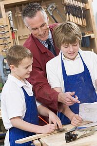 Male students reviewing woodworking plans with teacher