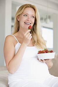 Pregnant woman with bowl of strawberries smiling