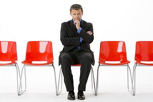 Businessman Sitting In Row Of Empty Chairs 
