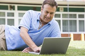 Man lying on lawn of school using laptop