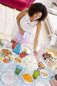 Woman at party putting candles in cake on food table smiling