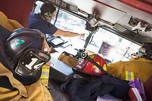 Two firefighters driving a fire engine with gear in the back (selective focus)