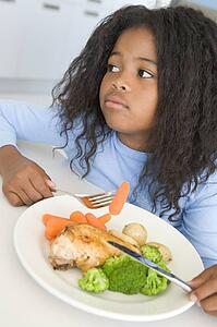 Young girl in kitchen eating chicken and vegetables