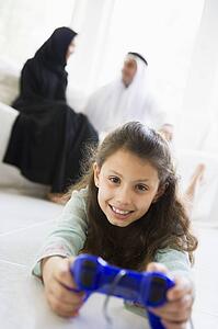 Daughter in living room playing video games smiling with parents in background (high key/selective focus)