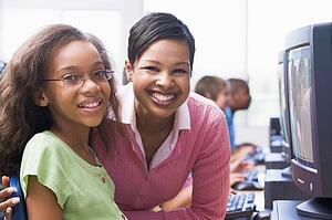 Teacher and student at computer terminal with students in background (selective focus/high key)