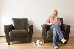 Woman sitting in chair with magazine on cellular phone smiling