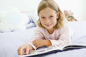 Young Girl Lying On Her Bed In Her Pajamas, Reading A Book