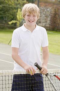 Young boy with racket on tennis court smiling