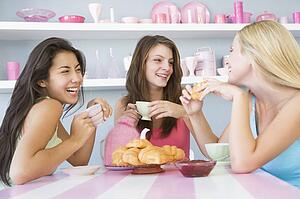 Three young woman sitting at a table having tea and a snack
