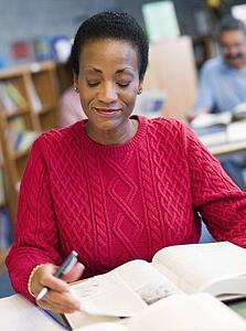 Woman sitting in library with a book and notepad (selective focus)