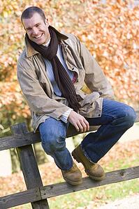 Man outdoors at park sitting on fence smiling (selective focus)