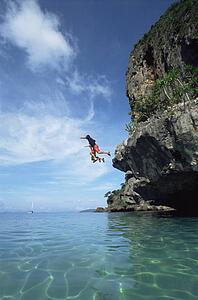 Couple outdoors jumping off cliff into ocean