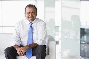 Businessman sitting indoors smiling (high key/selective focus)