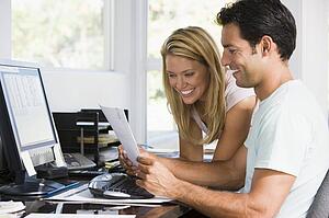 Couple in home office with computer and paperwork smiling