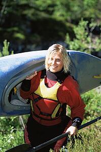Woman outdoors carrying small kayak and smiling (selective focus)